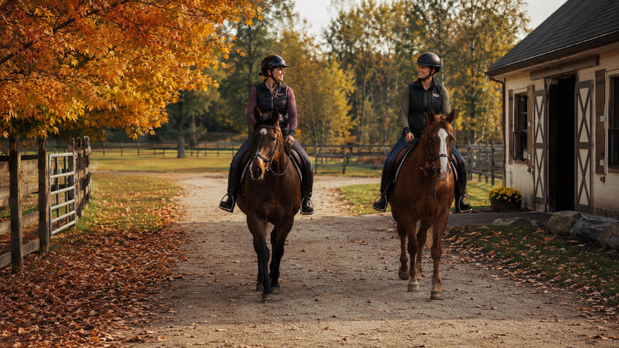 Two helmeted riders walking calm horses along an autumn barn trail