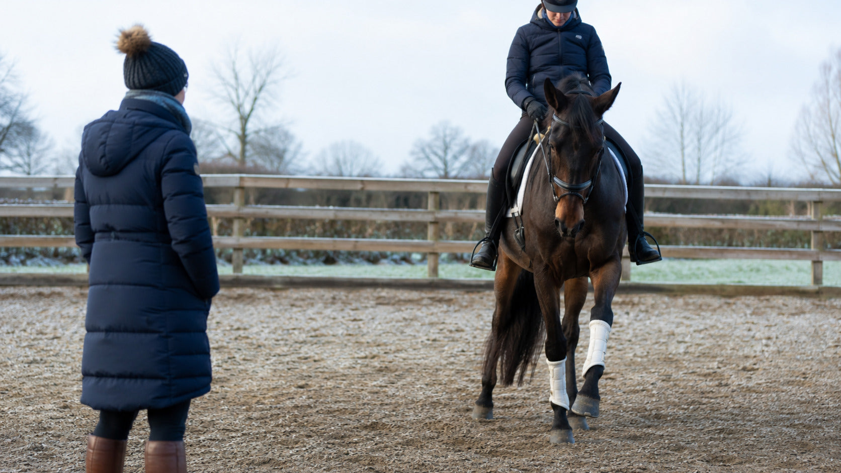 Horse and rider walking forward while a trainer observes shoulder movement on a cold morning