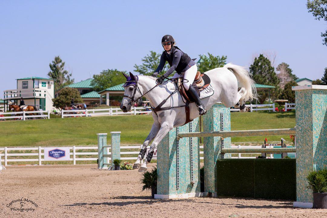 Evie Jaeckle competing over a show jump on a grey horse