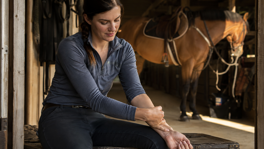 Working rider rubbing a tired forearm after barn chores beside a horse